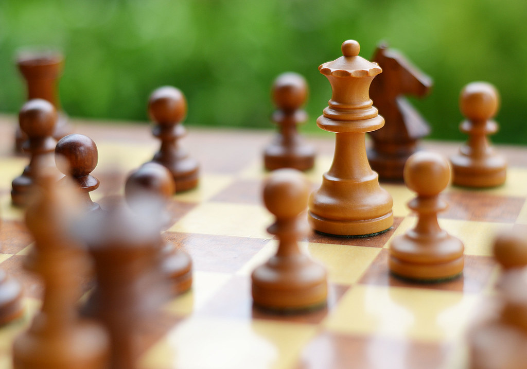 The white queen threatens a hanging black knight on a chess board in shallow focus